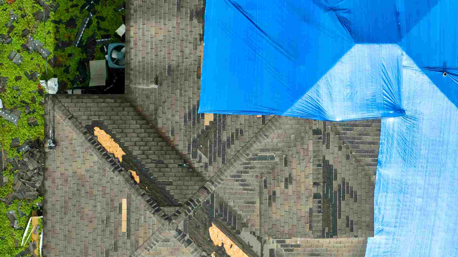 An aerial view of a hail-damaged roof covered with tarps